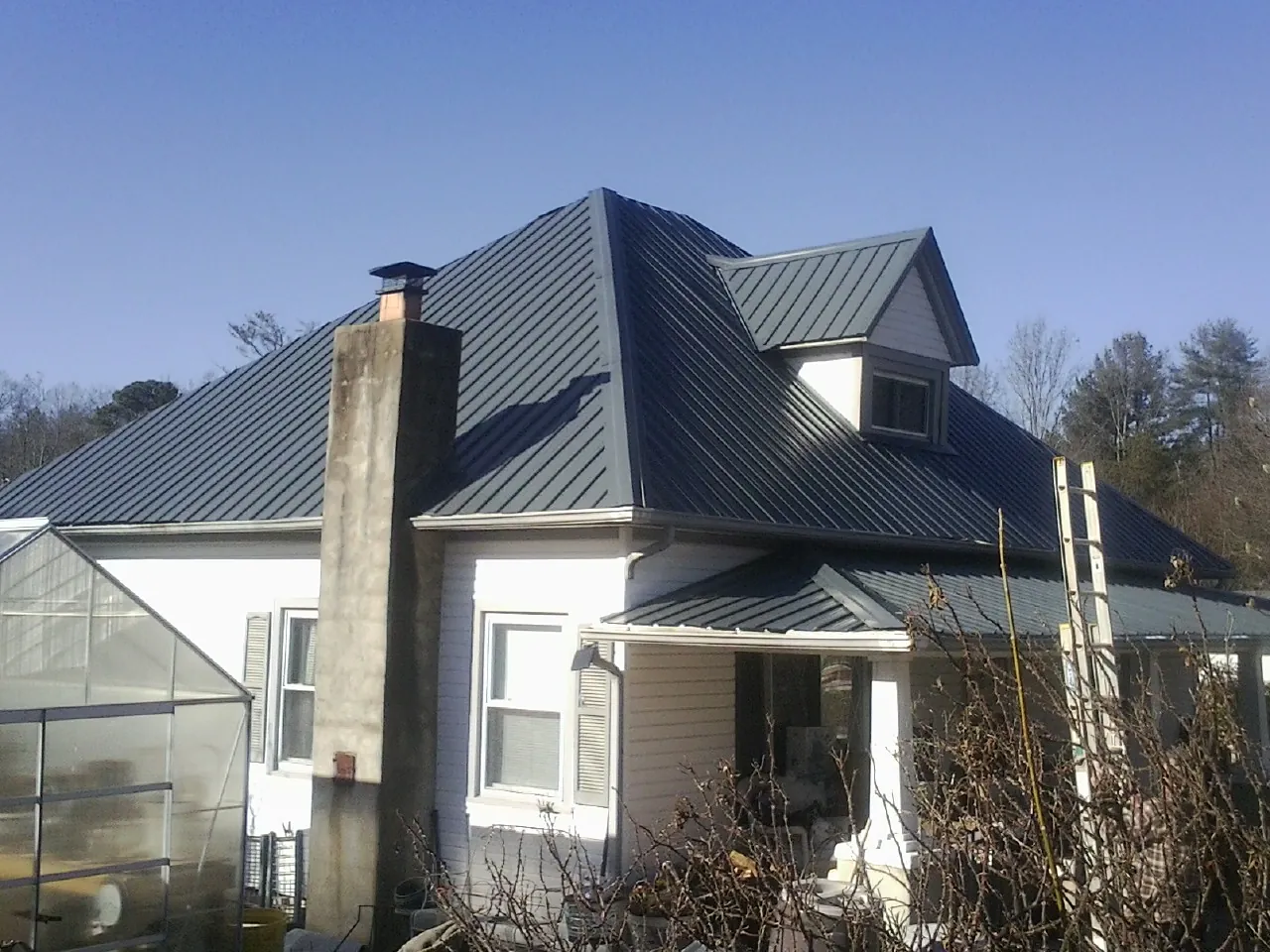 Dark blue standing seam metal roof on a white farmhouse with dormer — Slate & Tile Roof Repair by Roofing Brothers in Huffman