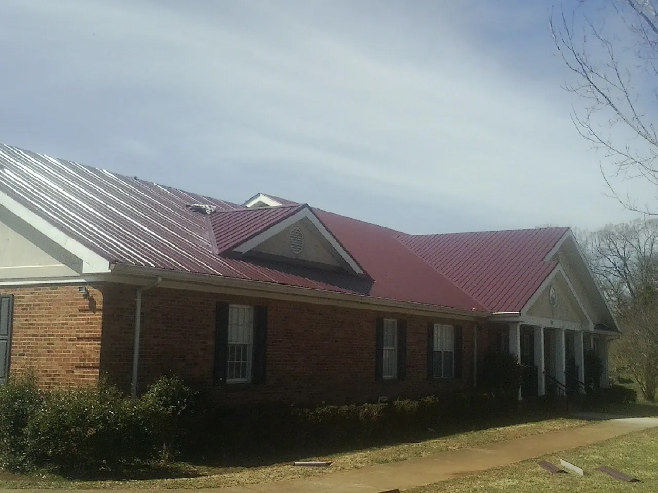 Red metal roof with gabled entries on a long brick building, from a Hail Damage Roof Repair job in Huffman