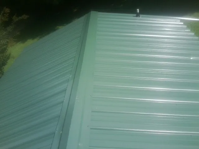 New green metal panels meeting at the ridge of a roof — Flat Roof Repair work by our crew in Huffman