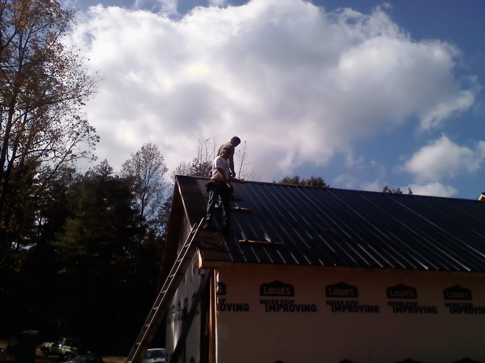 Roofer fastening dark metal panels high against a cloudy sky, from a Roof Inspection job in Huffman